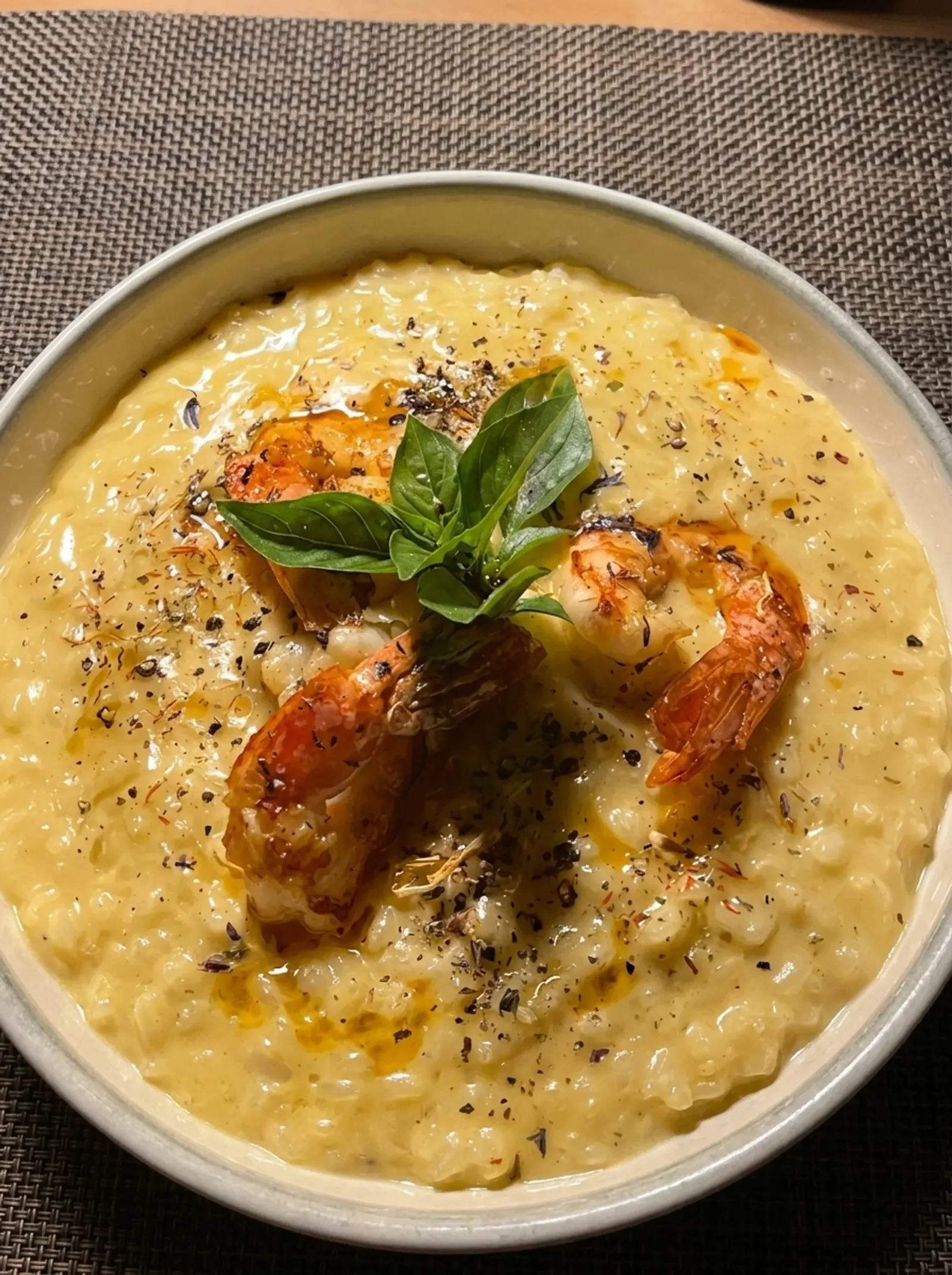 Shrimp on saffron risotto in a dark bowl, topped with basil and cracked pepper, shot from above.