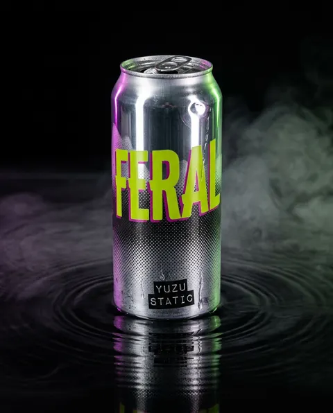 The same FERAL can on a dark reflective surface with green smoke behind it and a ripple around the base.